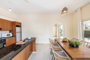 A modern kitchen with wooden cabinets, a microwave, and a dining area with wicker chairs and a wooden table. - Coralia Dream 1 - Three Bedroom Villa, Sleeps 6 (Peyia)
