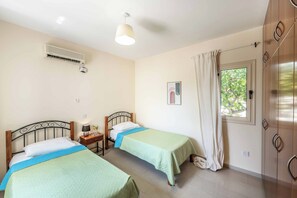 A bedroom with two beds, an air conditioning unit, a bedside table with a lamp, a framed picture on the wall, and a window with curtains. - Coralia Dream 1 - Three Bedroom Villa, Sleeps 6 (Peyia)