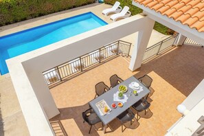 Zona de piscina en la azotea con una mesa lista para comer, rodeada de sillas.
