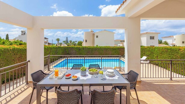 Eine Terrasse mit Blick auf einen Pool, einem Esstisch mit Stühlen und einem Geländer.