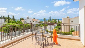 Ein Balkon mit Tisch und Stühlen, der auf ein Wohngebiet mit Häusern und einem klaren Himmel blickt.