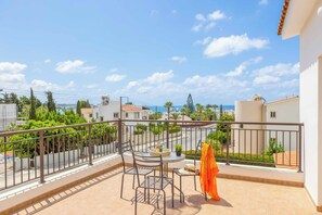 A balcony with a table and chairs, overlooking a residential area with houses and a clear sky. - Coralia Dream 1 - Three Bedroom Villa, Sleeps 6 (Peyia)