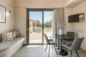 A modern living room with a sofa, a dining table with chairs, a TV mounted on the wall, and a sliding glass door leading to an outdoor patio. - Sea Melody - Two Bedroom Villa, Sleeps 4 (Ionian Islands)