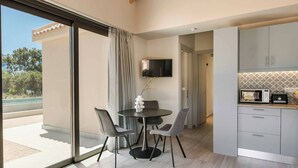 A modern kitchen with a built-in oven and microwave, a dining area with a round table and chairs, and a large sliding glass door leading to a balcony. - Sea Melody - Two Bedroom Villa, Sleeps 4 (Ionian Islands)