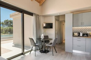 A modern kitchen with a built-in oven and microwave, a dining area with a round table and chairs, and a large sliding glass door leading to a balcony. - Sea Melody - Two Bedroom Villa, Sleeps 4 (Ionian Islands)