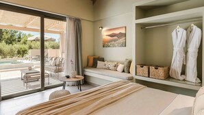 Ein modernes Schlafzimmer mit einem großen Bett, einer Sitzecke mit Blick ins Freie und einem Kleiderschrank mit Bademänteln.