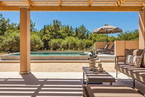 Ein überdachter Außenbereich mit Pool, Liegestühlen und einer Pergola.