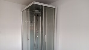 Un espace de douche d’angle doté d’une porte en verre, d’un pommeau de douche et d’un flexible de douche.