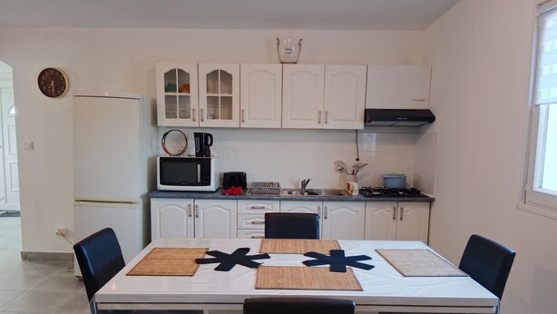 Une cuisine moderne avec des meubles blancs, un four à micro-ondes, une machine à café et une cuisinière à gaz. On y trouve une table à manger avec quatre chaises et deux sets de table.