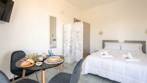 Una habitación de hotel con cama, una mesa de comedor con sillas, un televisor y un armario.