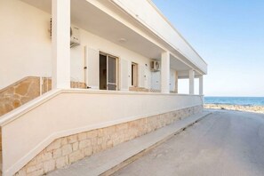 Ein Küstenhaus mit überdachter Veranda, Steinstufen und Blick aufs Meer.