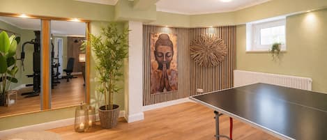 A room with a ping pong table, a large mirror, a Buddha statue, and a gym area.
