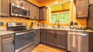 A modern kitchen with stainless steel appliances, wooden cabinets, and a window providing natural light. - 🎱 Riversong Elegance | Game Room, Hot Tub & Sleeps 12, Minutes to Dollywood 🏔️ (Sevierville)