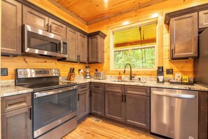 A modern kitchen with stainless steel appliances, wooden cabinets, and a window providing natural light. - 🎱 Riversong Elegance | Game Room, Hot Tub & Sleeps 12, Minutes to Dollywood 🏔️ (Sevierville)
