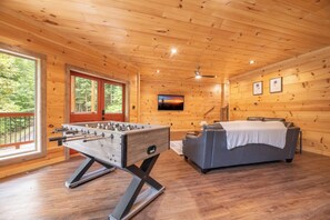 A wooden-floored room with a foosball table, a sofa, and a painting on the wall. - 🎱 Riversong Elegance | Game Room, Hot Tub & Sleeps 12, Minutes to Dollywood 🏔️ (Sevierville)