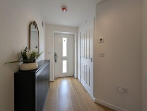 A hallway with a black console, a mirror, and a potted plant. There is a door with a window at the end. - 3-Bed Home | Sleeps 5 | Free Parking | Newcastle - Pass the Keys (Newcastle)