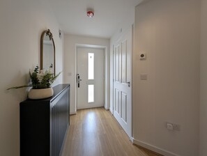 Ein Flur mit einer schwarzen Konsole, einem Spiegel und einer Topfpflanze. Am Ende ist eine Tür mit einem Fenster zu sehen.