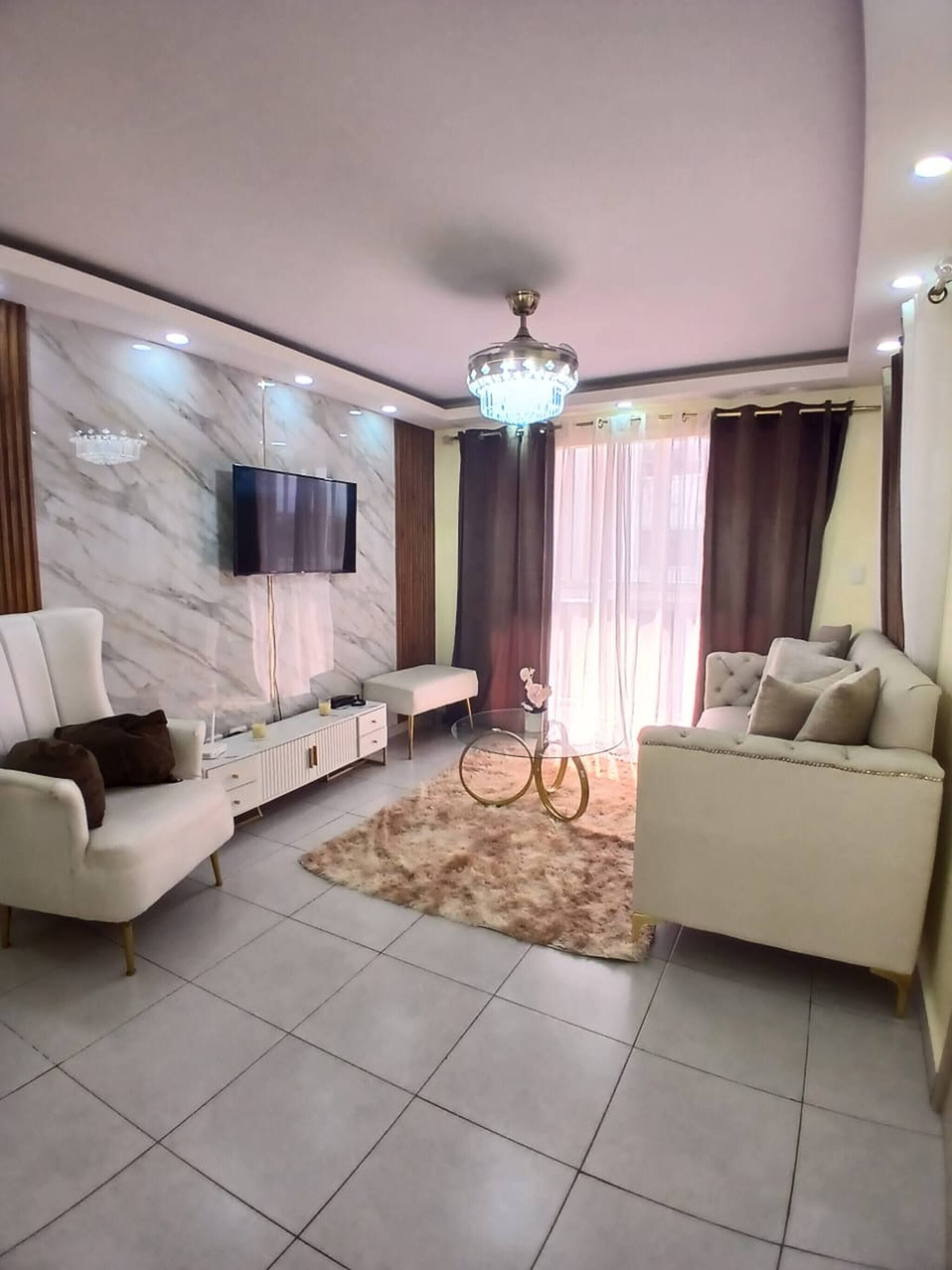A modern living room with a flat-screen TV, two sofas, a coffee table, and a chandelier.