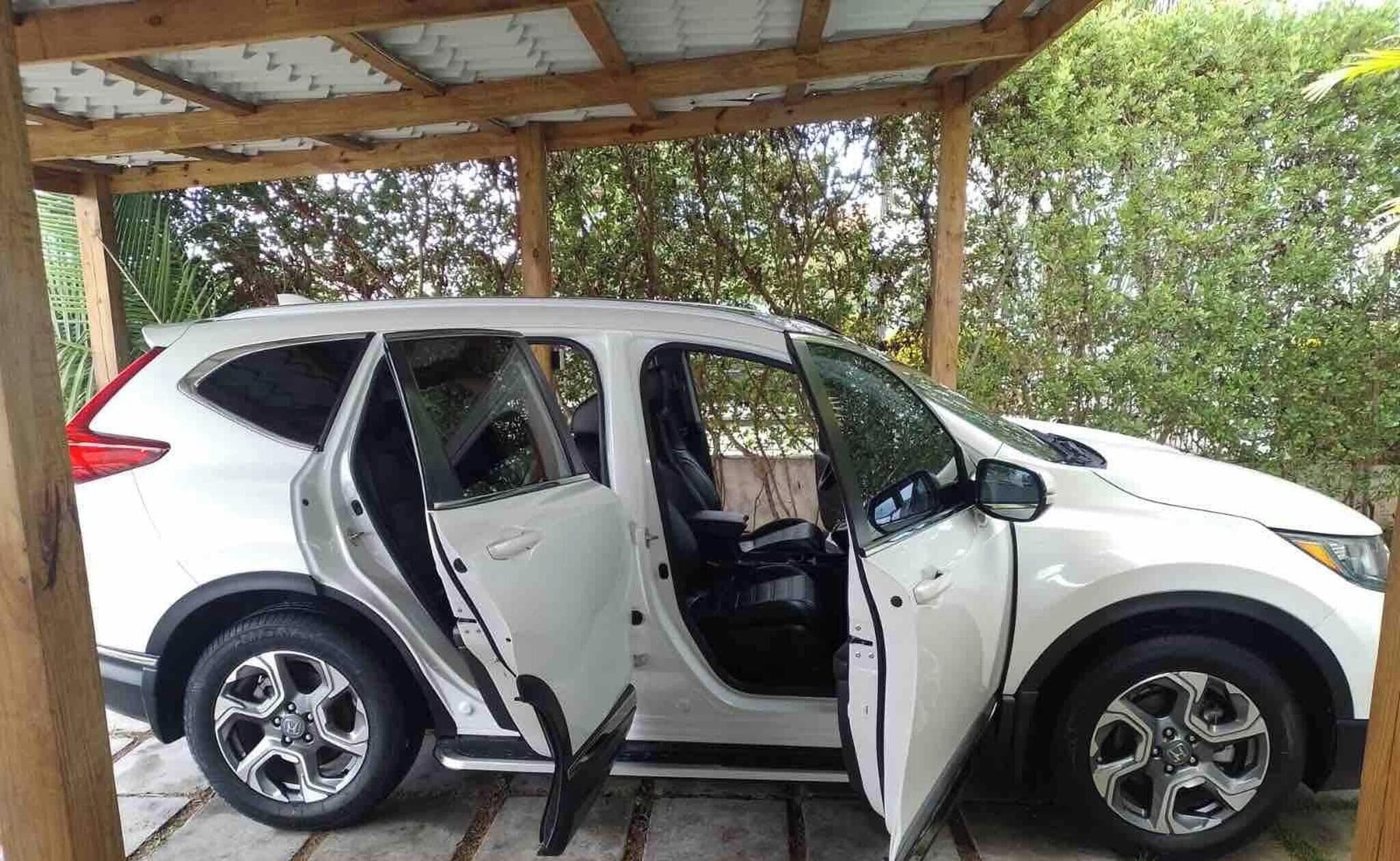Un SUV blanco estacionado bajo una estructura de madera con techo metálico, rodeado de follaje.
