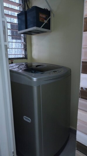 A compact, stainless steel washing machine in a corner of a room with a window and a black box labeled 'supertex' above it. - Beautiful 3 Bedroom Apartment With Pool on Av (Santo Domingo Norte)