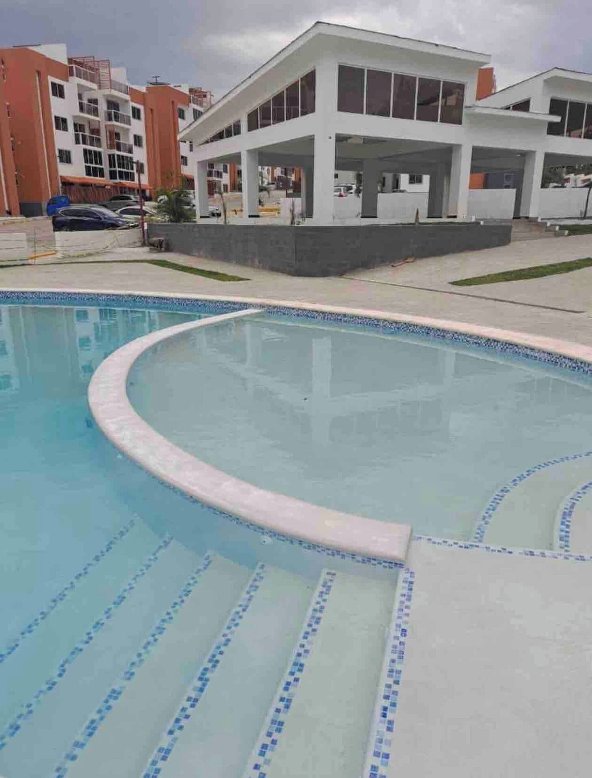 Ein Pool mit geschwungener Kante und blauen Fliesen, umgeben von einem Gebäude mit flachem Dach und großen Fenstern.