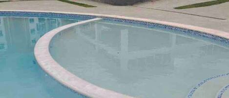 Ein Pool mit geschwungener Kante und blauen Fliesen, umgeben von einem Gebäude mit flachem Dach und großen Fenstern.