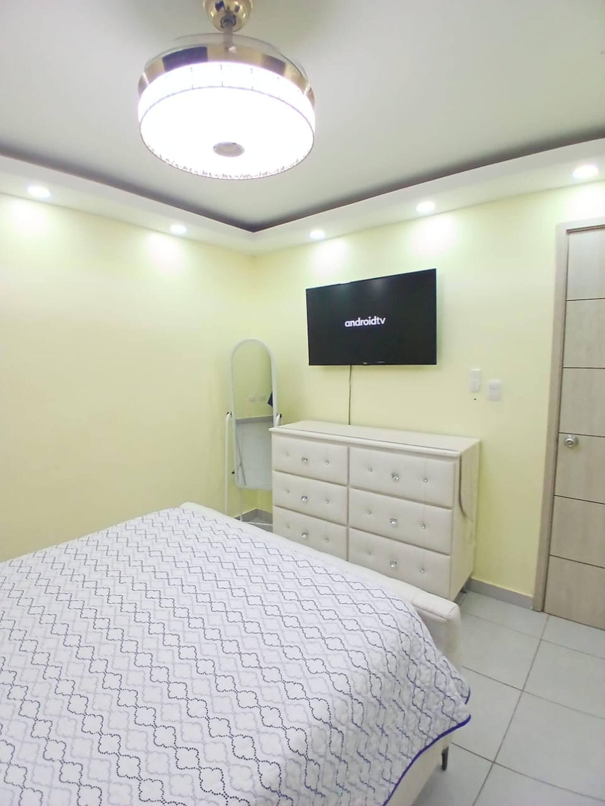 Une chambre à coucher comprenant un lit, une commode, un téléviseur et un luminaire fixé au plafond.