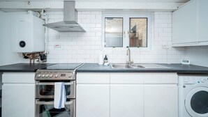 A modern kitchen with white cabinetry, a stainless steel range, an oven, a washing machine, and a window with a view of a brick building. - Camberwell house - with Central London bus links - Pass the Keys (London)