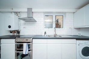 Eine moderne Küche mit weißen Schränken, einem Edelstahlherd, einem Backofen, einer Waschmaschine und einem Fenster mit Blick auf ein Backsteingebäude.