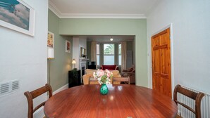 A dining room with a wooden table and chairs, a vase with flowers, and a living area with a sofa and a television. - Camberwell house - with Central London bus links - Pass the Keys (London)
