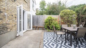 A patio with a patterned rug, a wooden table, and chairs. - Camberwell house - with Central London bus links - Pass the Keys (London)