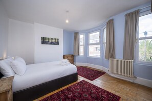 A bedroom with a bed, a nightstand, a radiator, and a window with curtains. - Camberwell house - with Central London bus links - Pass the Keys (London)