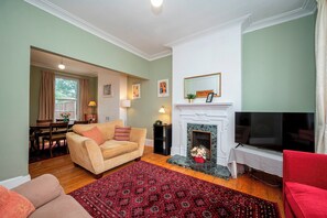 Un salon avec un canapé beige, un tapis à motifs rouges, une cheminée et un téléviseur.