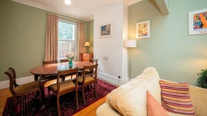A dining area with a wooden table and chairs, a window with curtains, a lamp, and a sofa with cushions. - Camberwell house - with Central London bus links - Pass the Keys (London)