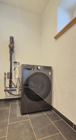 A compact, modern laundry room with a front-loading washing machine, a hose, and a control panel.