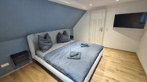 A bedroom with a bed, pillows, a TV mounted on the wall, and a door.