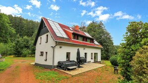 Een huis met een schuin dak, een overdekt terras en een oprit van grind.