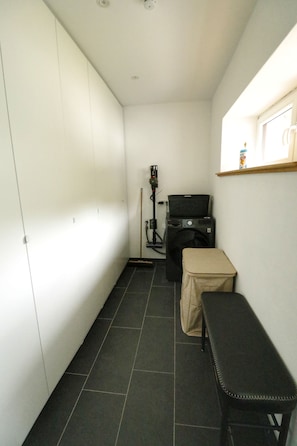 A narrow hallway with a washing machine, a bench, and a shelf with items on it.
