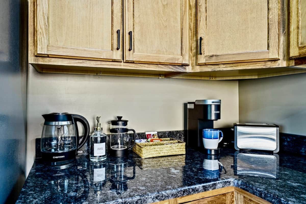 A kitchen with wooden cabinets, a coffee maker, a kettle, a toaster, and a coffee grinder on the counter.