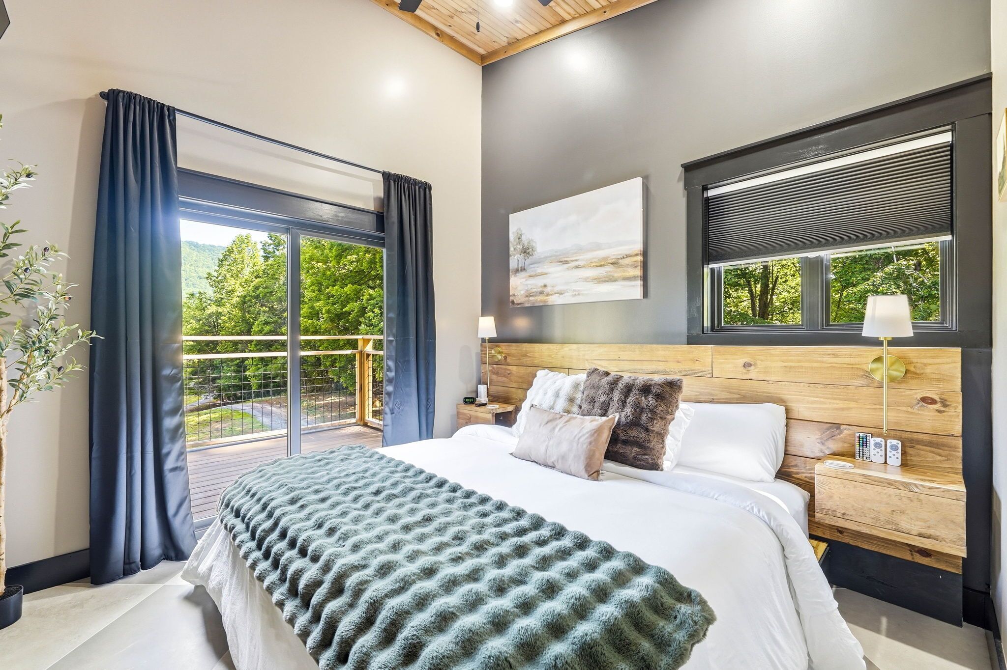 Une chambre moderne avec un grand lit, une tête de lit en bois, une vue sur la verdure par la fenêtre et un balcon agrémenté de rideaux.