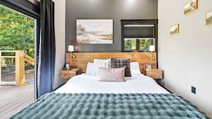 A modern bedroom with a large bed, wooden headboard, and a view of greenery outside. - Lovely 1-bedroom cabin with a hot tub in the mountains of Elizabethton (Elizabethton)