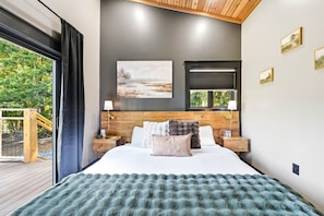 A modern bedroom with a large bed, wooden headboard, and a view of greenery outside. - Lovely 1-bedroom cabin with a hot tub in the mountains of Elizabethton (Elizabethton)