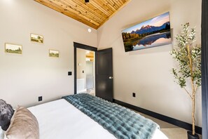 A bedroom with a bed, a wooden ceiling, a painting of a landscape, and a potted plant. - Lovely 1-bedroom cabin with a hot tub in the mountains of Elizabethton (Elizabethton)