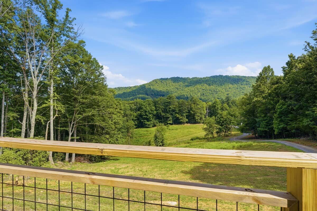 A wooden deck with a metal railing overlooking a green landscape with trees and a hill in the distance.