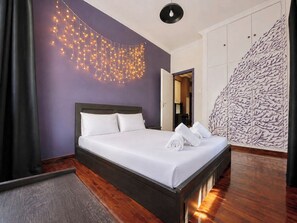 A hotel room with a bed, a wall-mounted light fixture, a wardrobe, and a patterned wall. - Transit Hub Pad - Steps to Metro -Sleeps 3 by ΜΡS (Athina)