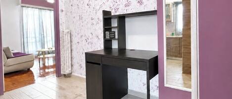 A modern room with a black desk, a white radiator, and a view of a kitchen through a mirror.