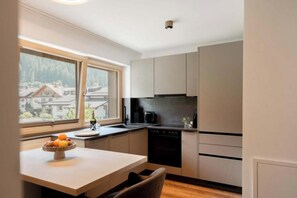 A modern kitchen with a dining area, a view of a mountain, and a window with a view of buildings. - Goldifor 22 Apartment (Gaschurn)