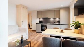 A modern kitchen with built-in appliances, a dining area with a table and chairs, and a living area with a sofa and a coffee table. - Grappeskopf 23 Apartment (Gaschurn)