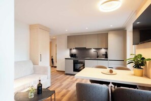 A modern kitchen with built-in appliances, a dining area with a table and chairs, and a living area with a sofa and a coffee table. - Grappeskopf 23 Apartment (Gaschurn)