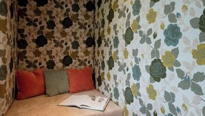 A corner of a room with floral patterned wallpaper, a beige sofa with three cushions, and an open book on the sofa. - Grappeskopf 23 Apartment (Gaschurn)